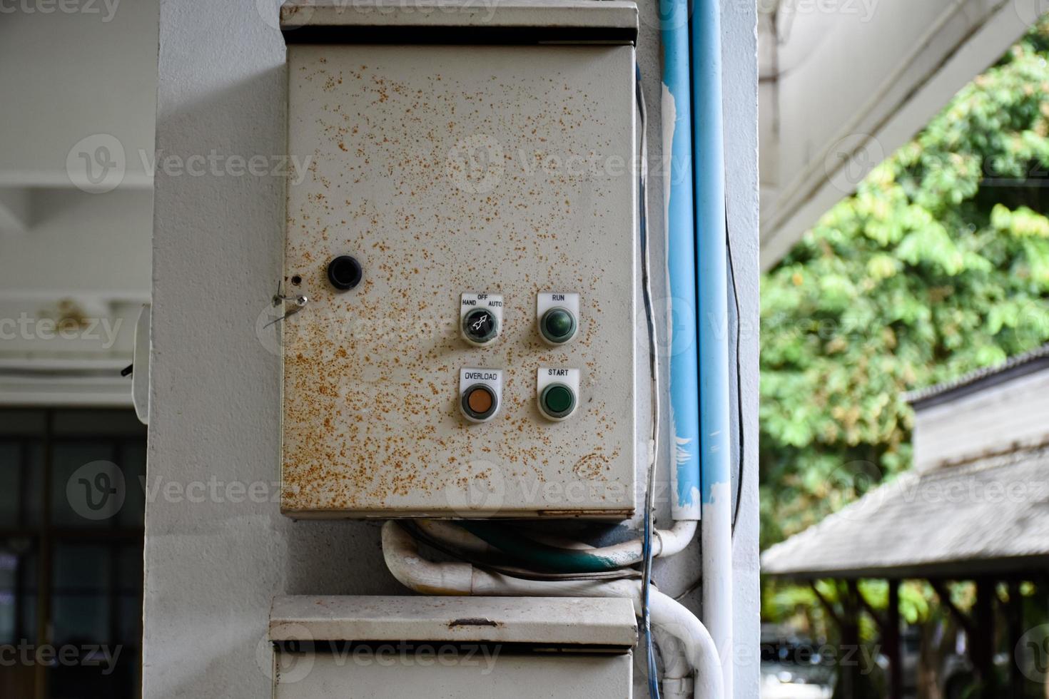 Metal box for controlling the turning on and turning off the water pump electrical system used in the building hanging on the wall, there is rust on the front surface of the lid of the box. photo