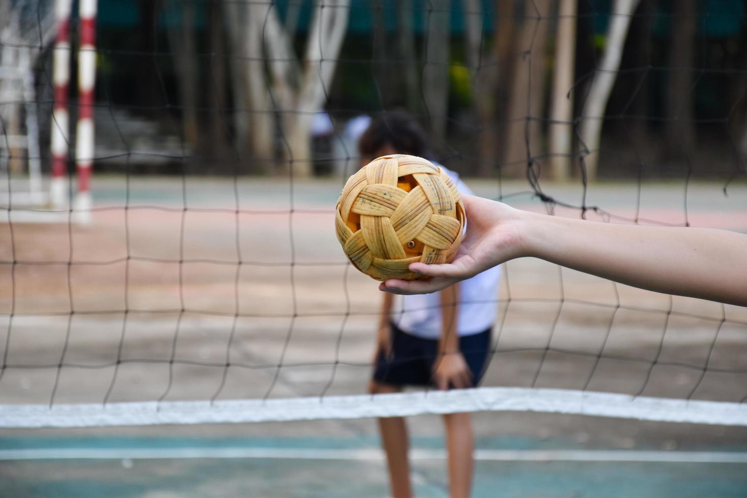 Sepak takraw ball, southeast asian countries traditional sport, holding in hand of young asian female sepak takraw player in front of the net before throwing it to another player to kick over the net. photo