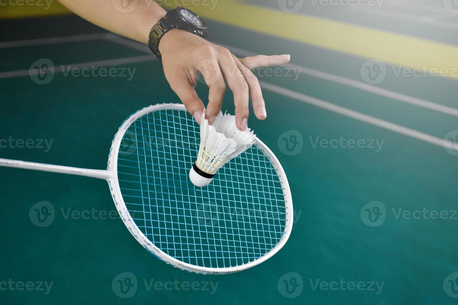 Badminton player holds racket and white cream shuttlecock in front of the net before serving it to another side of the court. photo