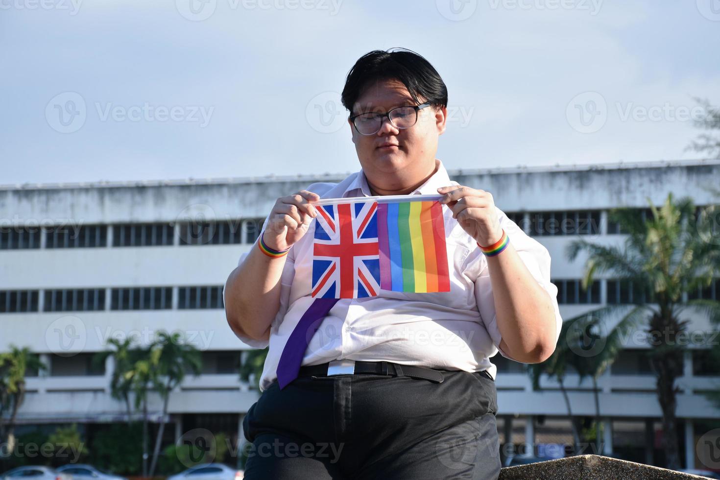 Asian boy holds rainbow flag and union jack flag and wears neck tie and standing outside the building, soft and selective focus, concept for lgbtq celebration in pride month. photo