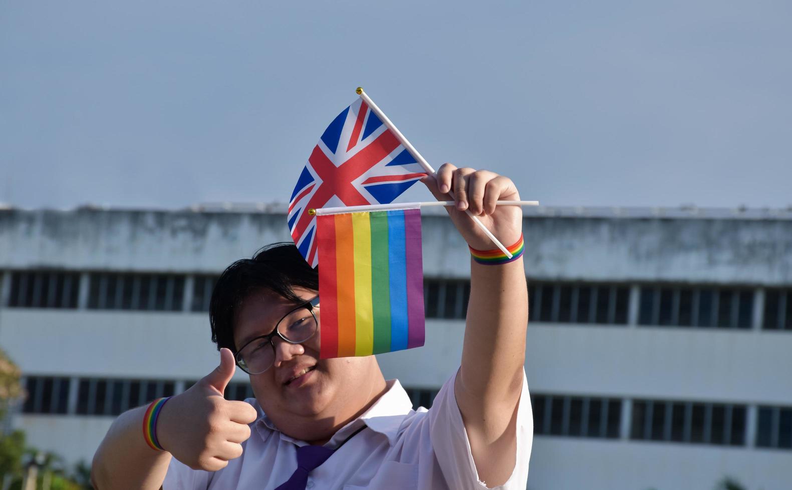 Asian boy holds rainbow flag and union jack flag and wears neck tie and standing outside the building, soft and selective focus, concept for lgbtq celebration in pride month. photo