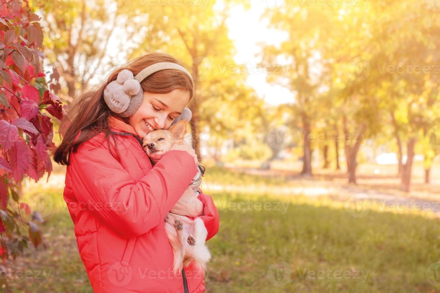 una adolescente con una chaqueta naranja con un perro chihuahua en los brazos. la niña abraza a su perro. foto