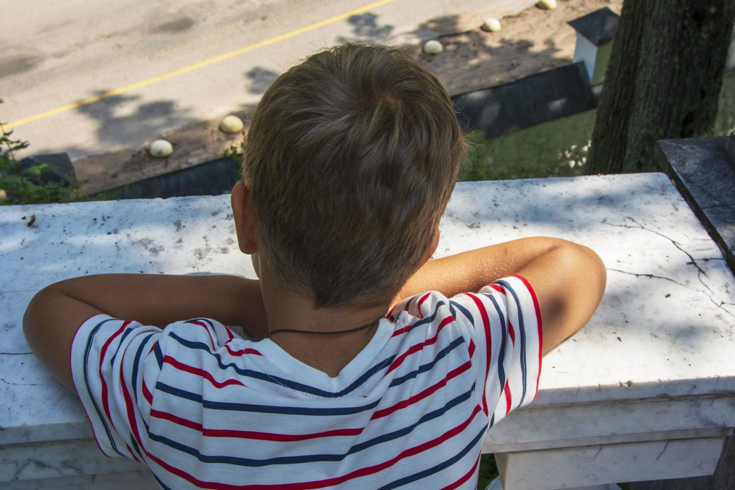 A preschooler looks down from the balcony, rear view. The concept of isolation and loneliness of young children photo