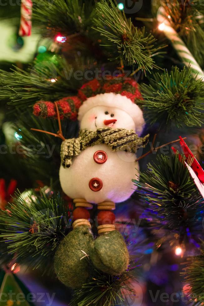 muñeco de nieve de fieltro en un abeto con adornos navideños y luces borrosas. foto