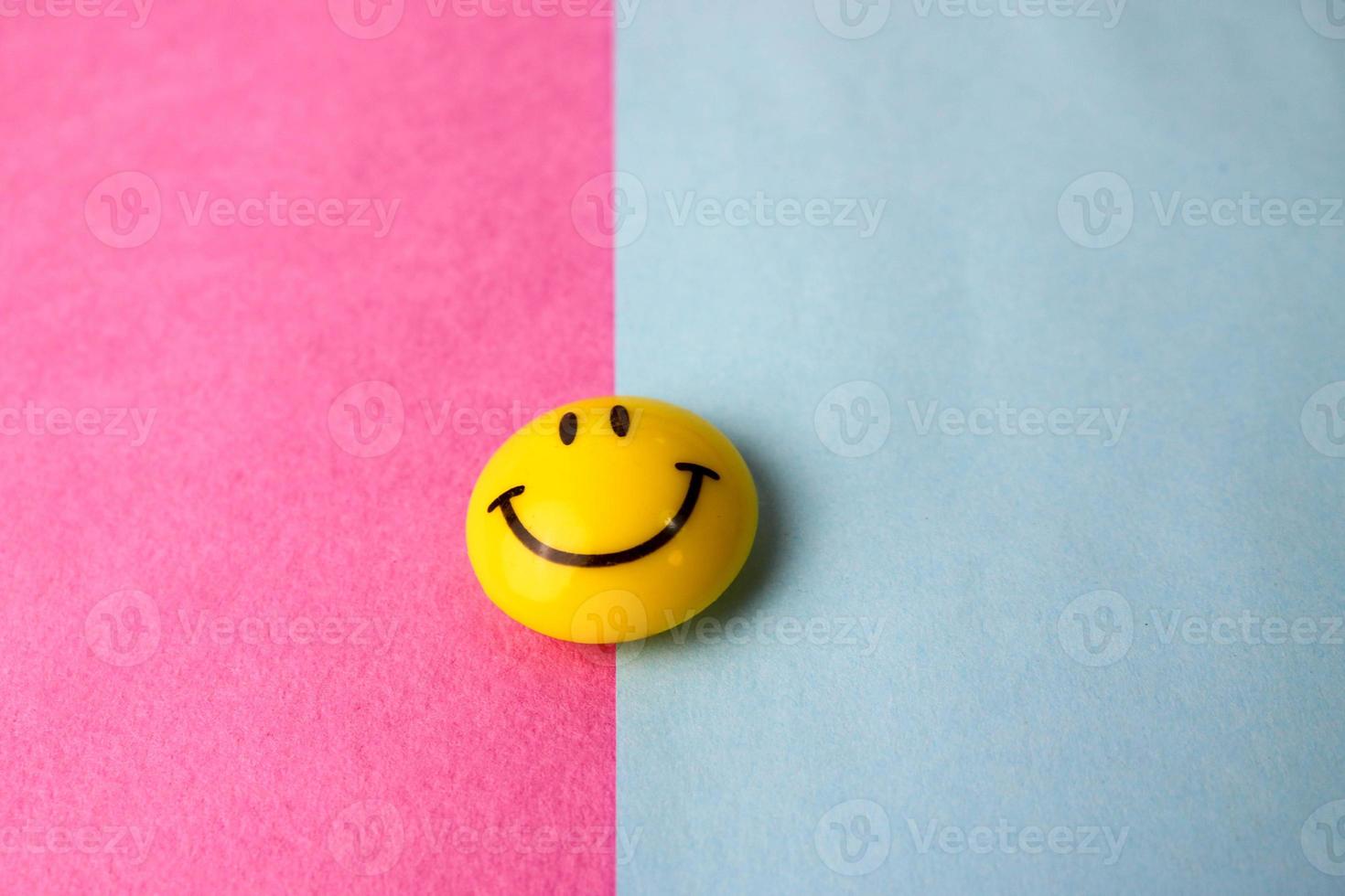 plástico redondo amarillo alegre sonriente juguete sonriente cara redonda emoji sobre un fondo rosa azul violeta foto