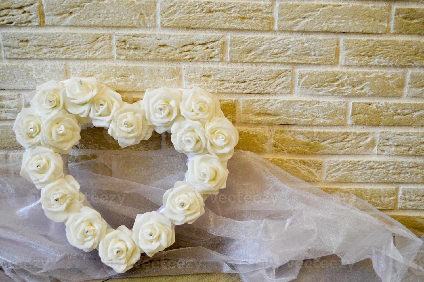 White heart with white roses and diamonds. Background of beige bricks. White transparent fabric. photo