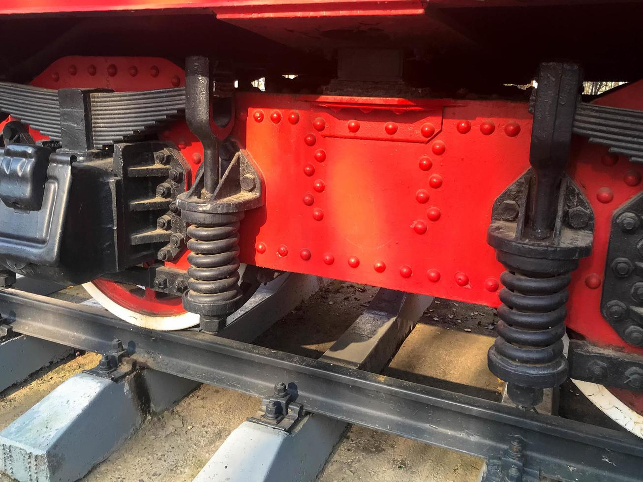 Large iron wheels of a red and black train standing on rails and suspension elements with springs of an old industrial steam locomotive photo