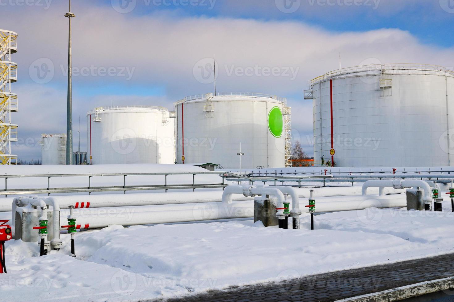 grandes tanques industriales de metal de hierro blanco para almacenamiento de combustible, gasolina y diesel y tuberías con válvulas y bridas en la refinería en invierno foto
