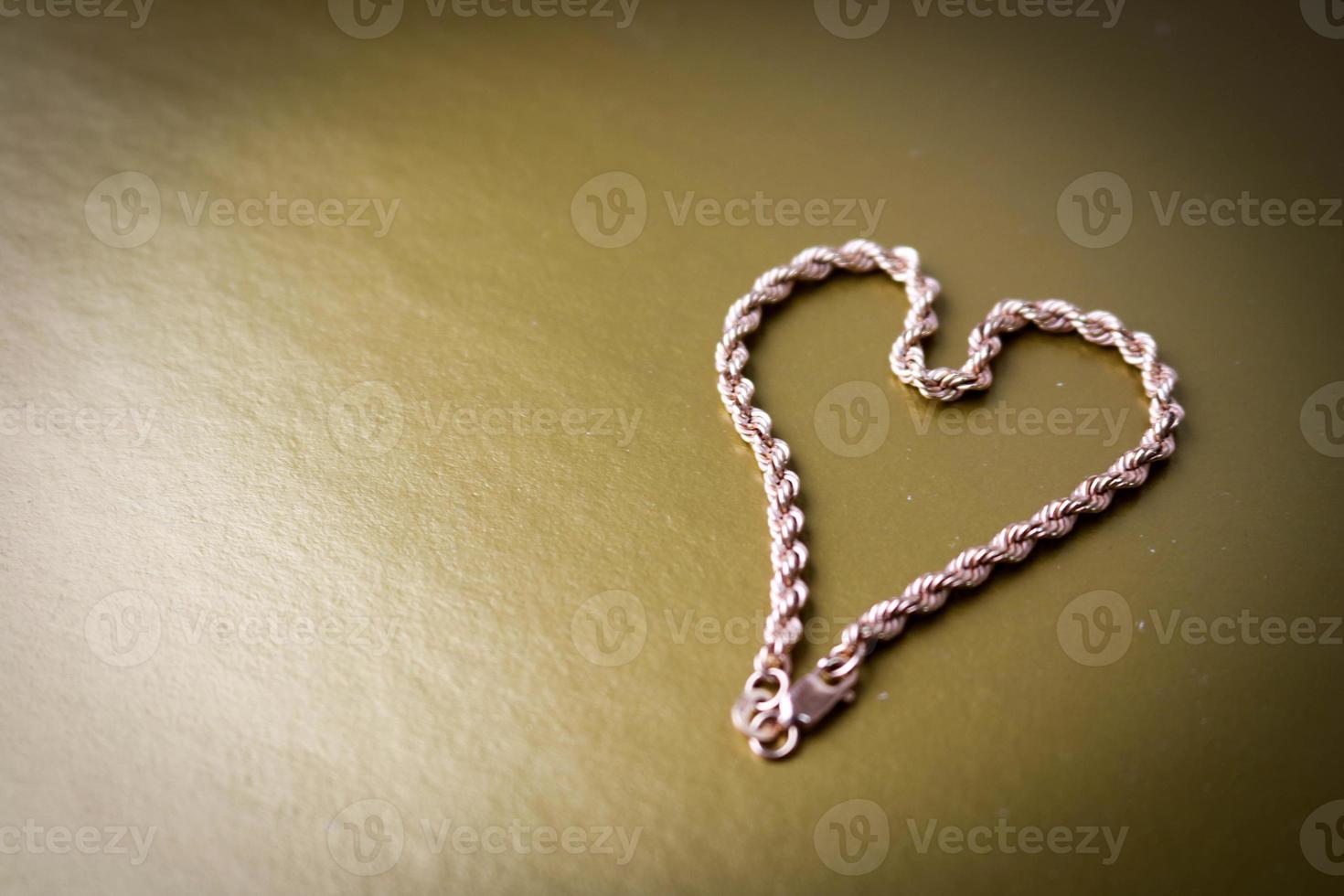 Texture of a beautiful golden festive chain unique weaving in the shape of a heart on a yellow gold background and copy space. Concept love, marriage proposal, marriage, St. Valentine's Day photo