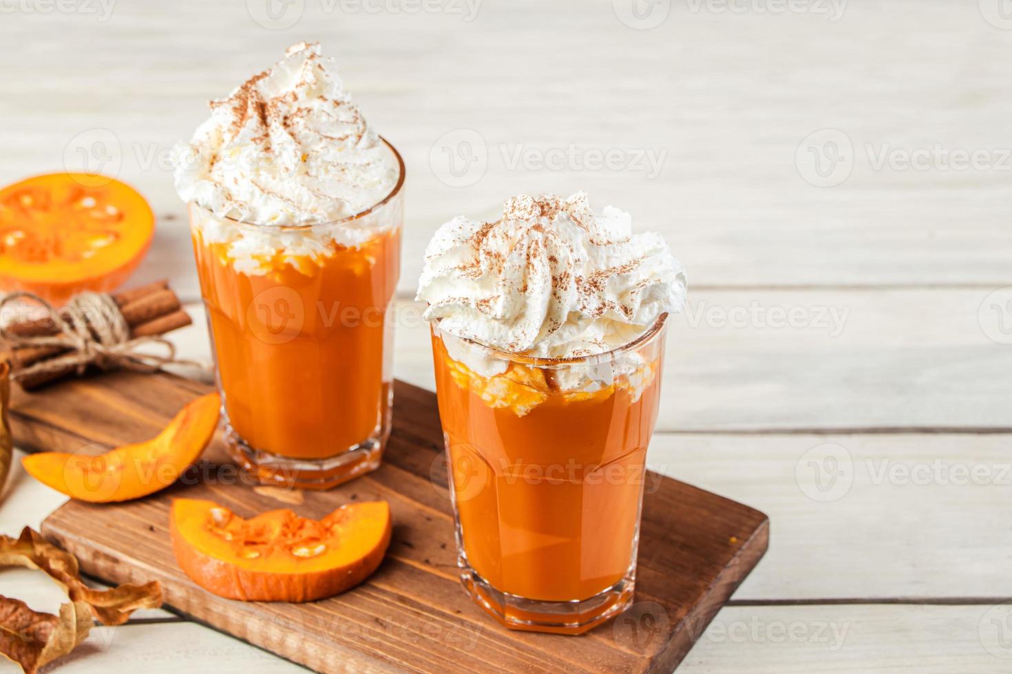 Spicy latte with pumpkin and whipped cream on wooden background. Hot coffee in glass mug and autumn leaves. photo