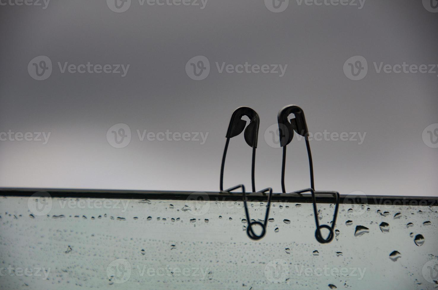 Safety pin couple sitting on glass wall with customizable space for text and ideas. Love and romance concept photo