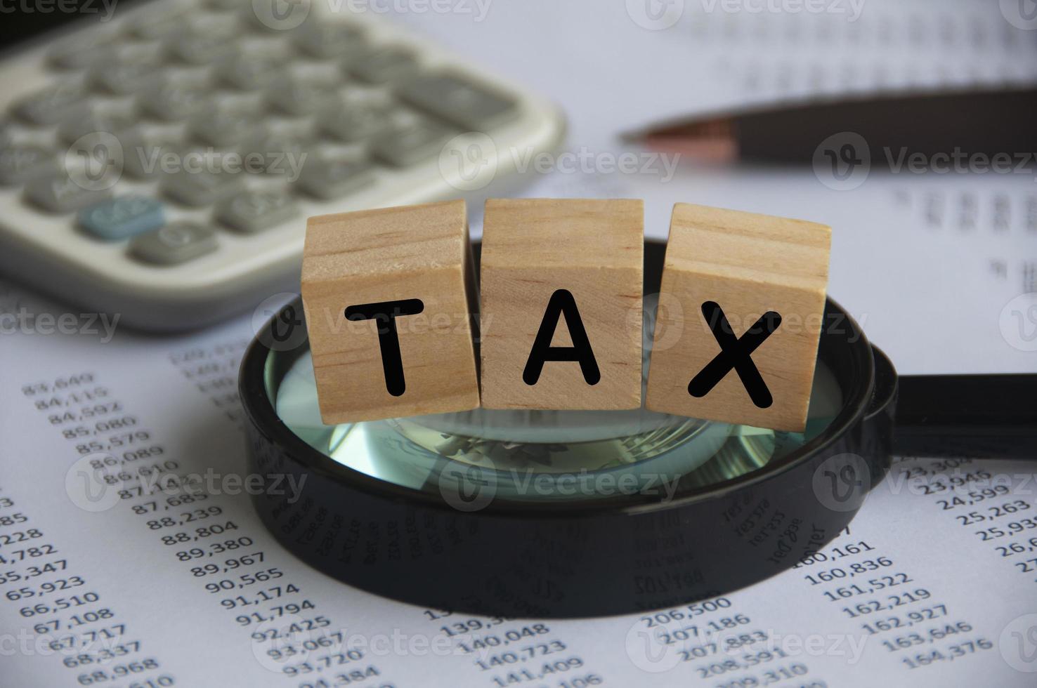 Tax word labeled wooden blocks on magnifying glass. Tax investigation concept.calculator and number analysis background. Tax concept photo