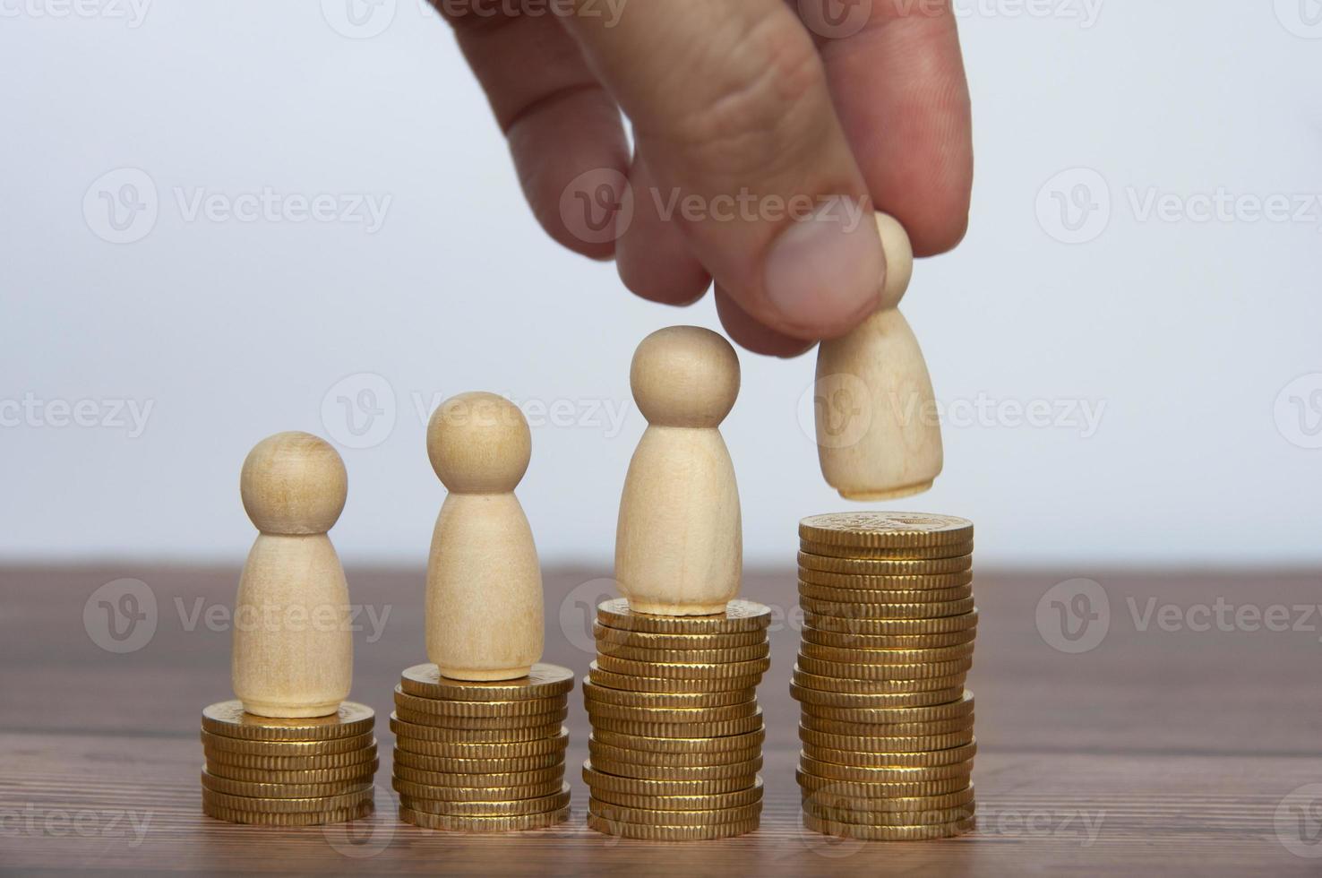 Hand placing wooden people figure on top of gold coins. Goal achievement, business growth and career progression photo