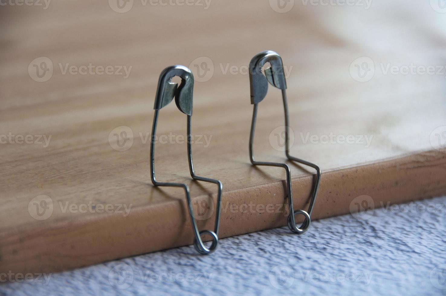 Two safety pins sitting on brown wood having a conversation. Friendship concept photo