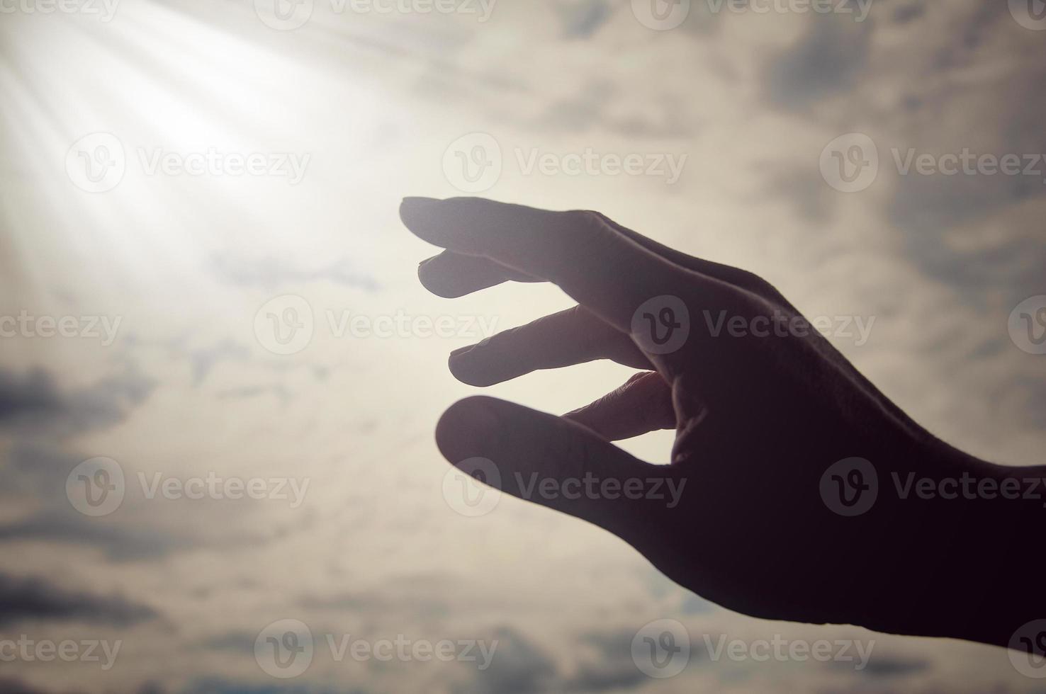 Hand reaching out to bright shining light on sky above. Religious and spiritual concept photo