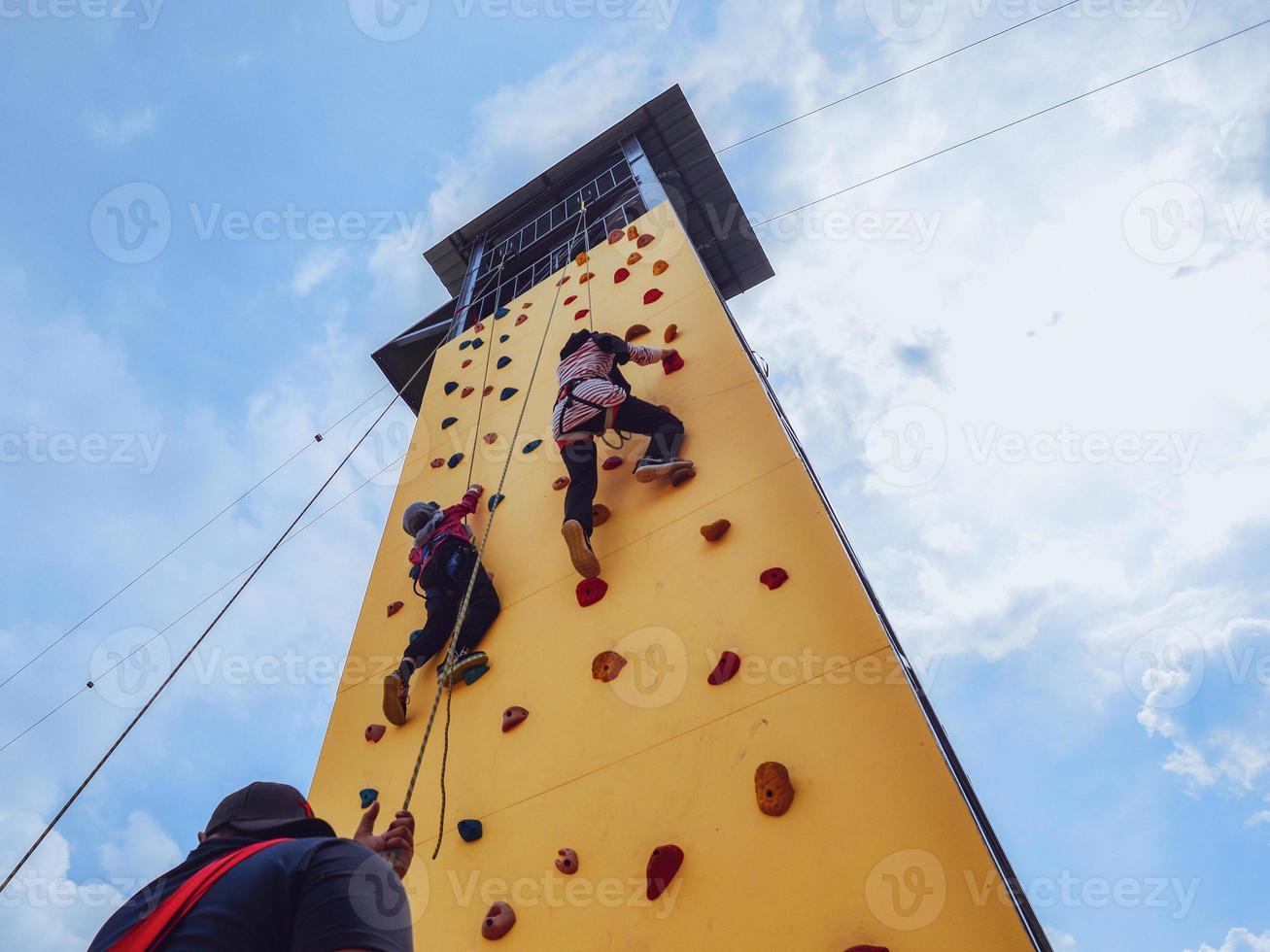 Two youth ascending up the yellow outdoor climbing tower photo