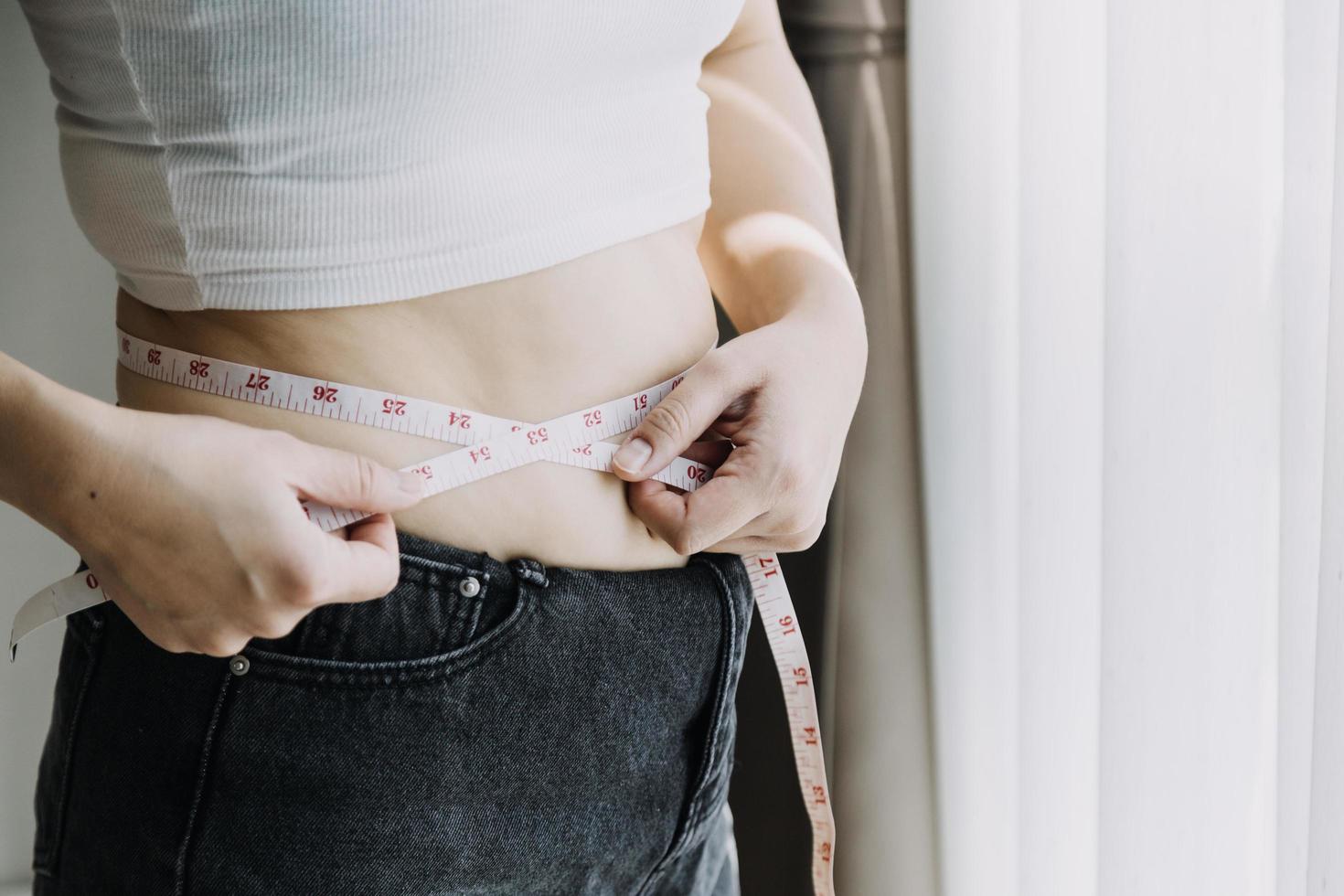 hermosa mujer gorda con cinta métrica usa su mano para exprimir el exceso de grasa que está aislado en un fondo blanco. ella quiere perder peso, el concepto de cirugía y descomponer grasa bajo el foto