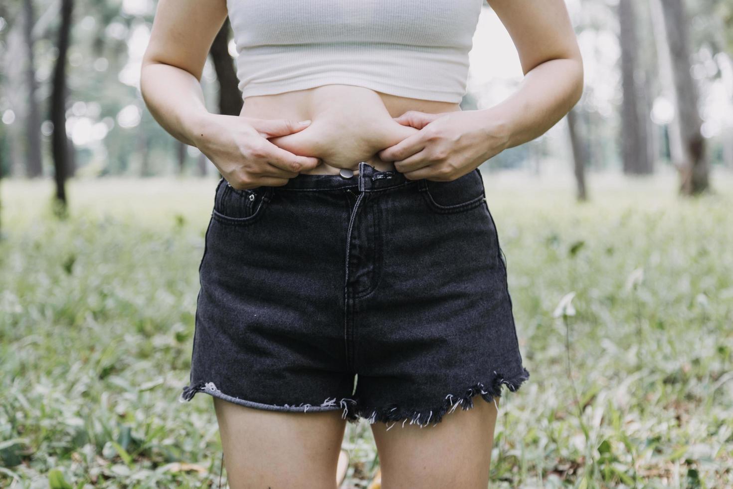 hermosa mujer gorda con cinta métrica usa su mano para exprimir el exceso de grasa que está aislado en un fondo blanco. ella quiere perder peso, el concepto de cirugía y descomponer grasa bajo el foto