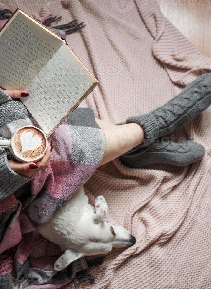 Cozy home, woman covered with warm blanket, drinks coffee,  sleeping dog next to woman. photo