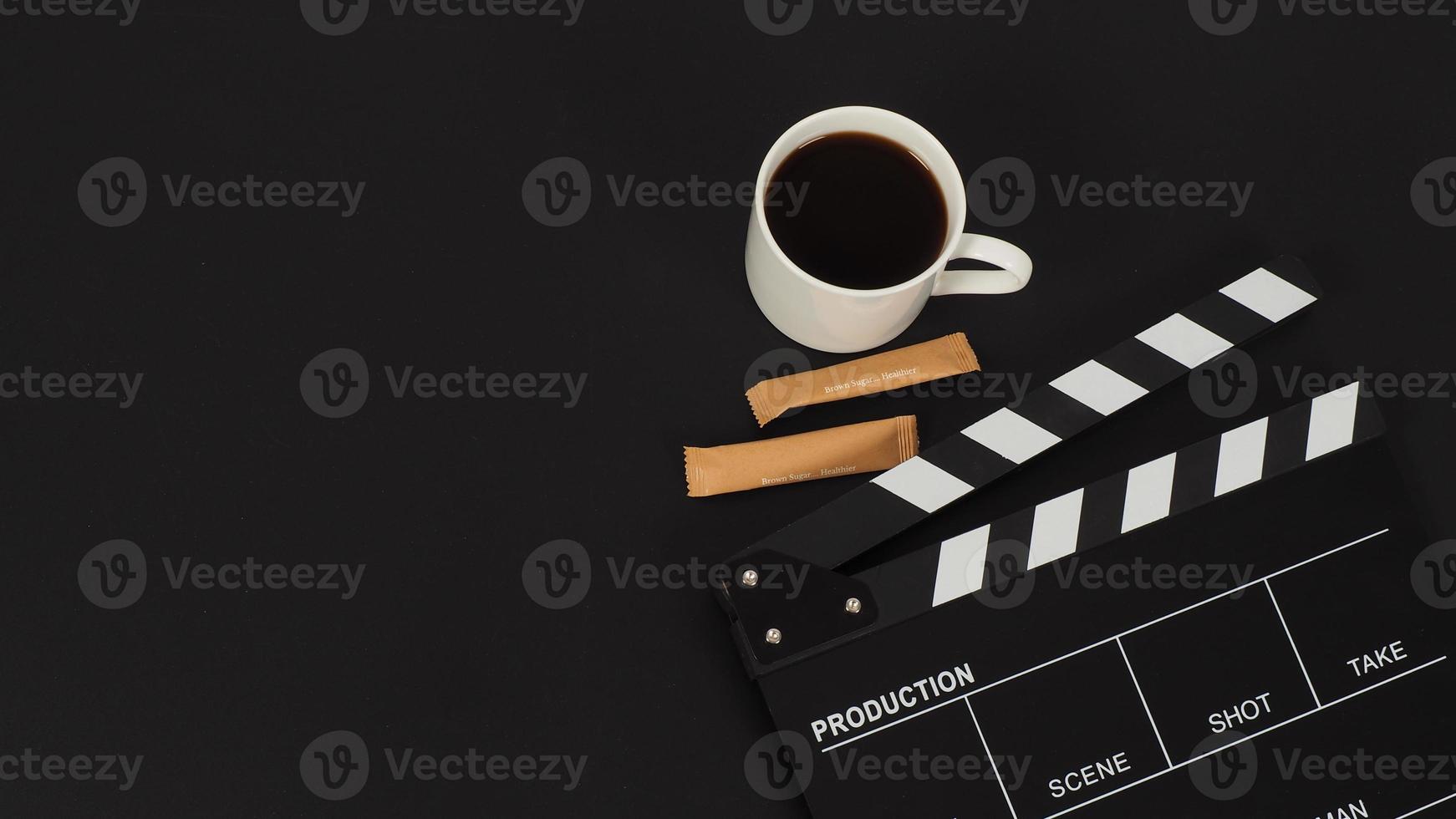 Black Clapper board and hot coffee white cup and two brown sugar sachet  on black background. photo