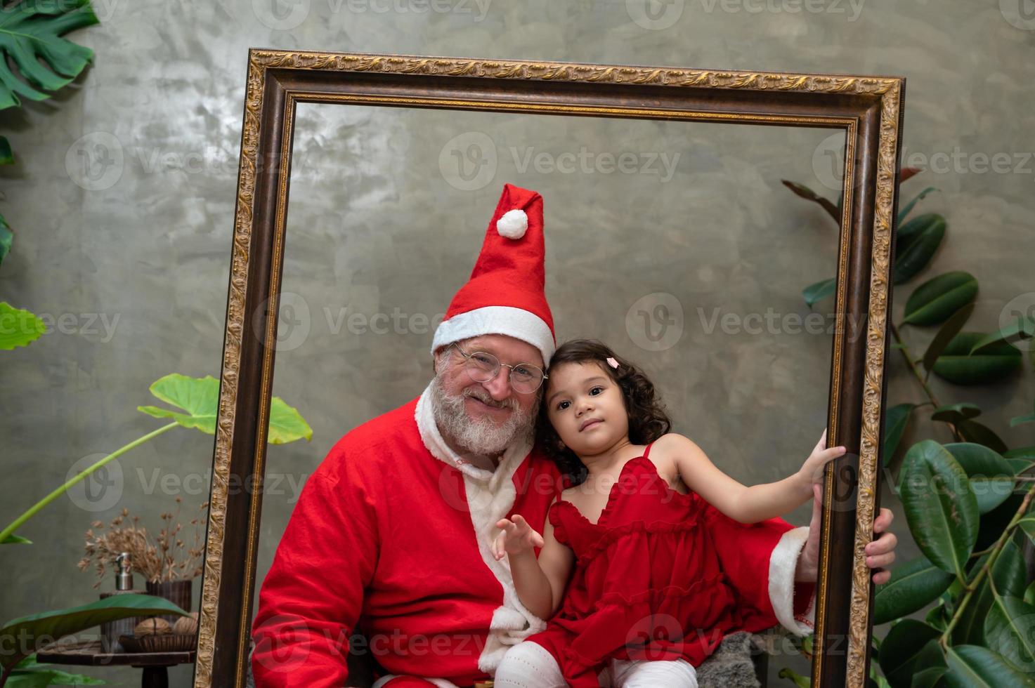 Santa Claus and cute little girl looking through picture frame photo