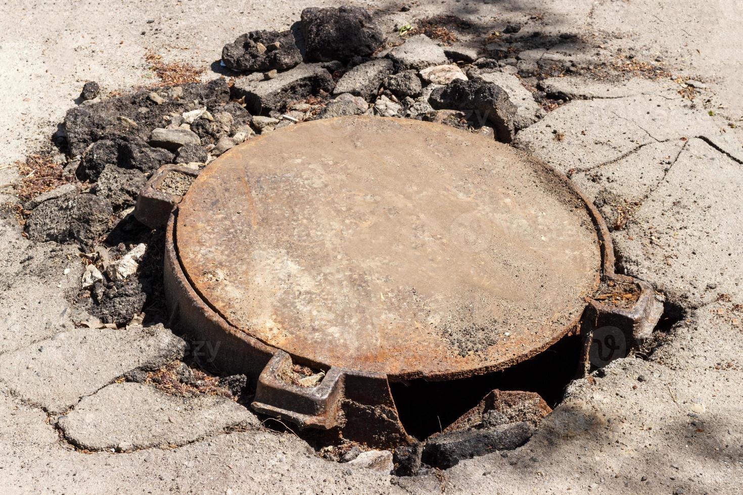 broken metal sewer hatch in the middle of an asphalt road photo