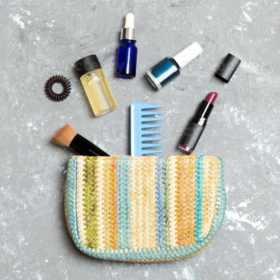 Make up products spilling out of cosmetics bag, on grey cement background with empty space for your design photo