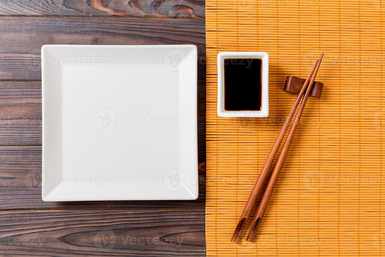 Empty white square plate with chopsticks for sushi and soy sauce on wooden background. Top view with copy space photo