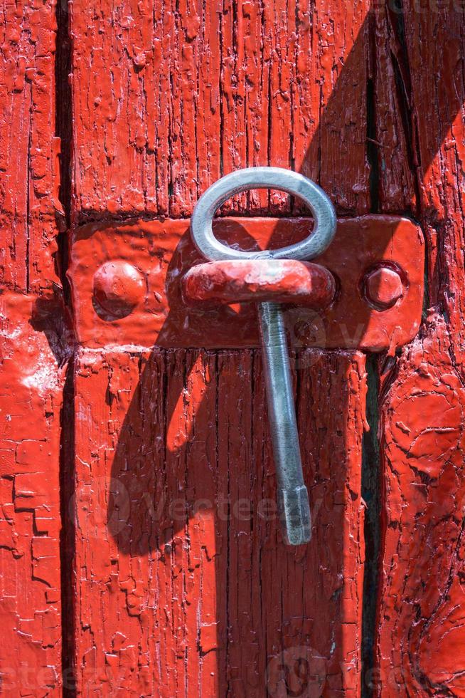 Antique iron key from a gate on a background of old red wooden gate. photo