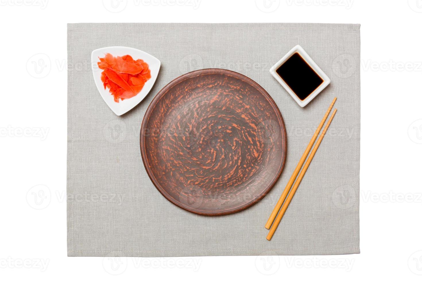 Empty round brown plate with chopsticks for sushi, ginger and soy sauce on grey napkin background. Top view with copy space for you design photo