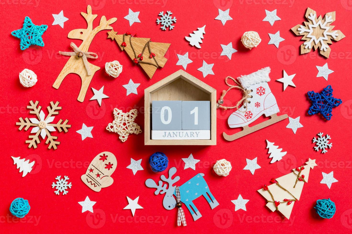 Top view of wooden calendar, holiday toys and decorations on red Christmas background. The first of January. New Year time concept photo
