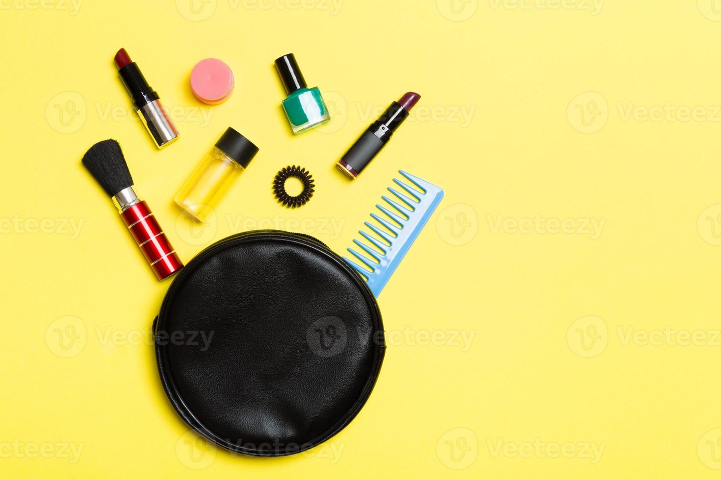 Top view of make up products fallen out of cosmetics bag on yellow background. Cosmetic concept with space for your design photo