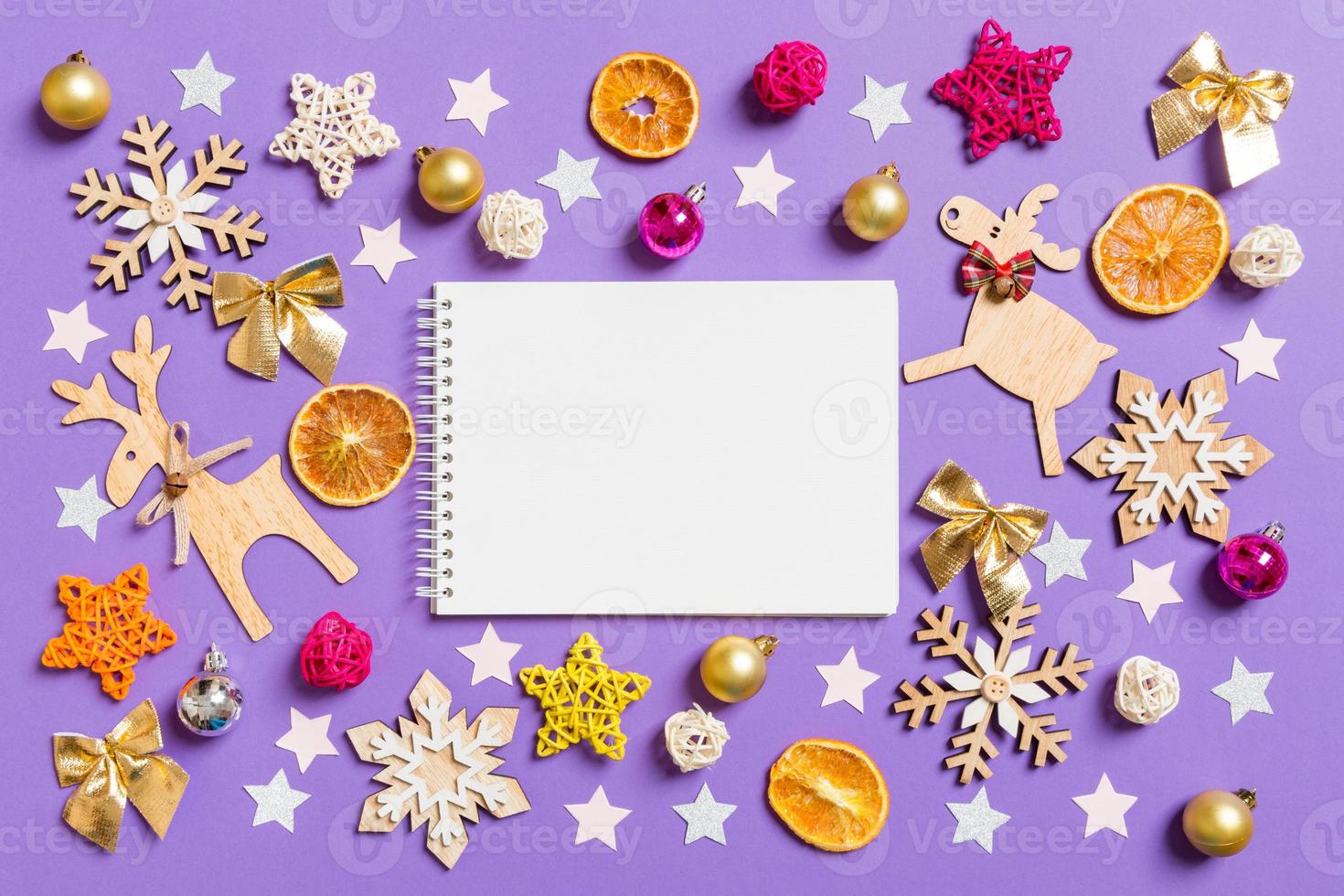 Top view of notebook surrounded with New Year toys and decorations on purple background. Christmas time concept photo