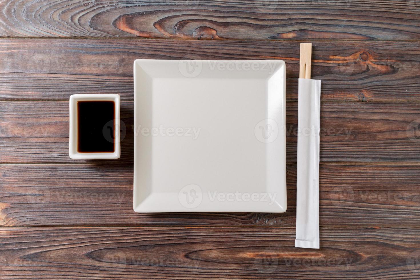 Empty white square plate with chopsticks for sushi and soy sauce on wooden background. Top view with copy space photo