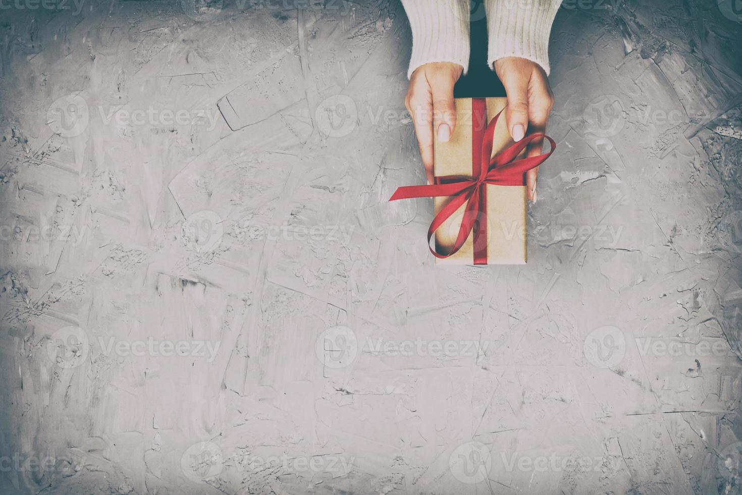 las manos de las mujeres dan San Valentín envuelto u otro regalo hecho a mano en papel con cinta roja. caja de regalo, decoración de regalo en mesa de cemento blanco, vista superior con espacio de copia foto