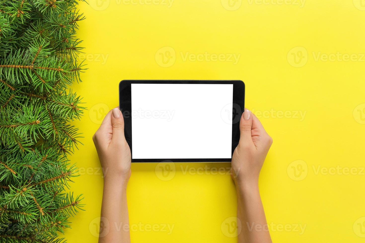 female hands with tablet computer on yellow christmas background. Xmas tree branch top view photo