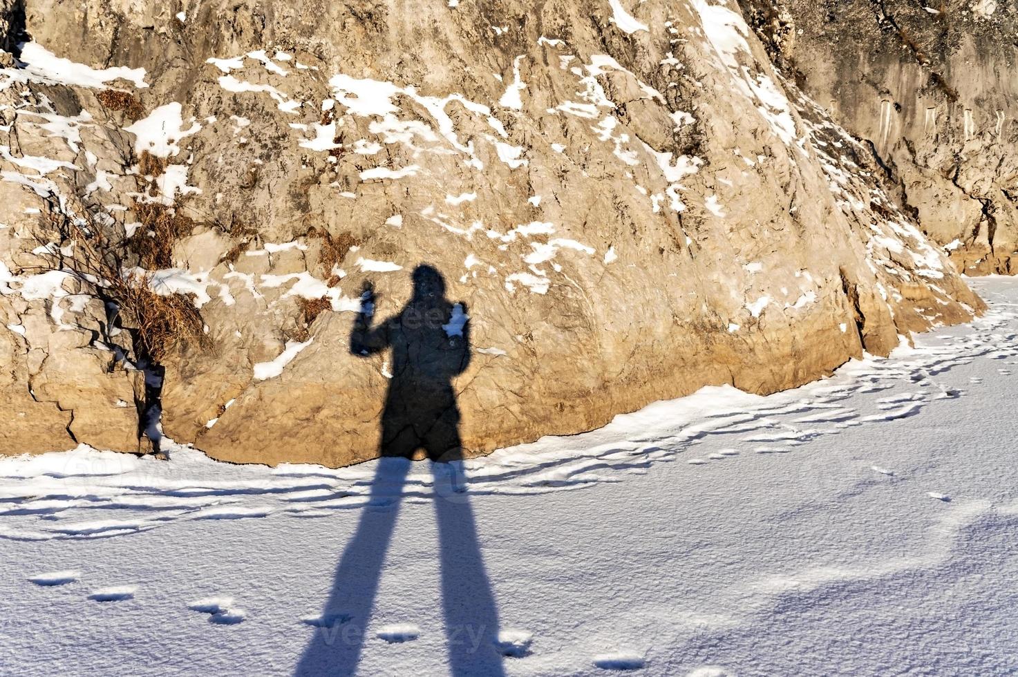 female shadow with long legs and a raised hand on fresh snow and a rock on a winter sunny day. Abstract photo