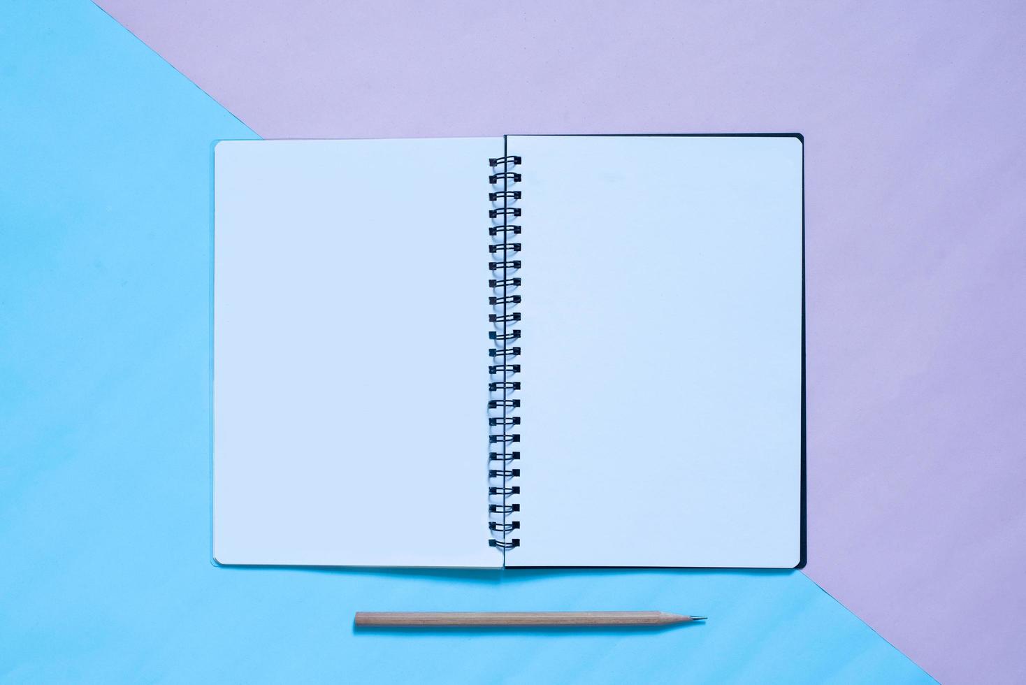 Top view of notebook and pencil on blue and pinl pastel color bakcground photo