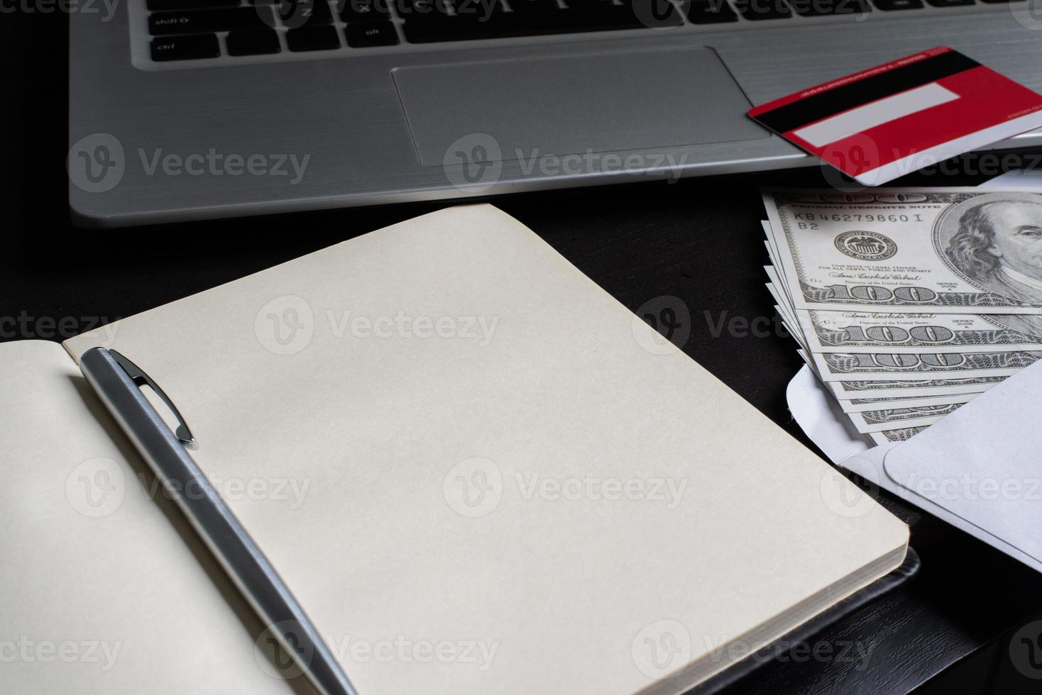 An open notebook with credit card, pen, dollars and laptop photo
