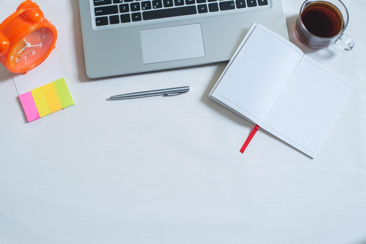 Top view of laptop, cup of tea, open notebook, pen, colorful mini paper note, orange clock photo