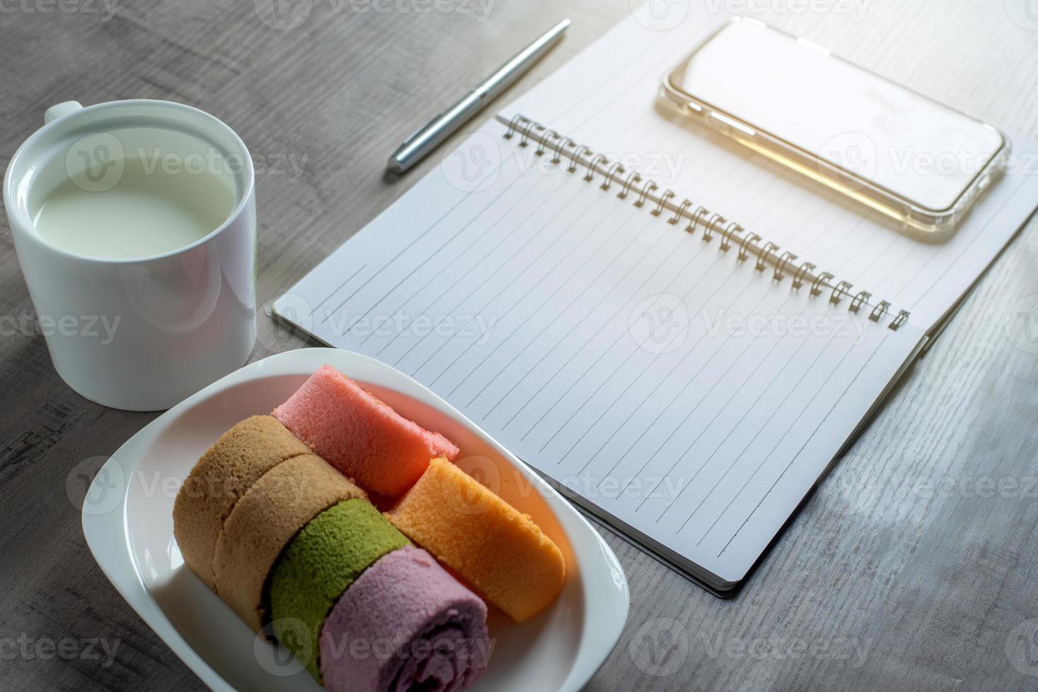 Notebook, smartphone, jam roll, cup of milk, pen on wooden, Business, education concept and design photo