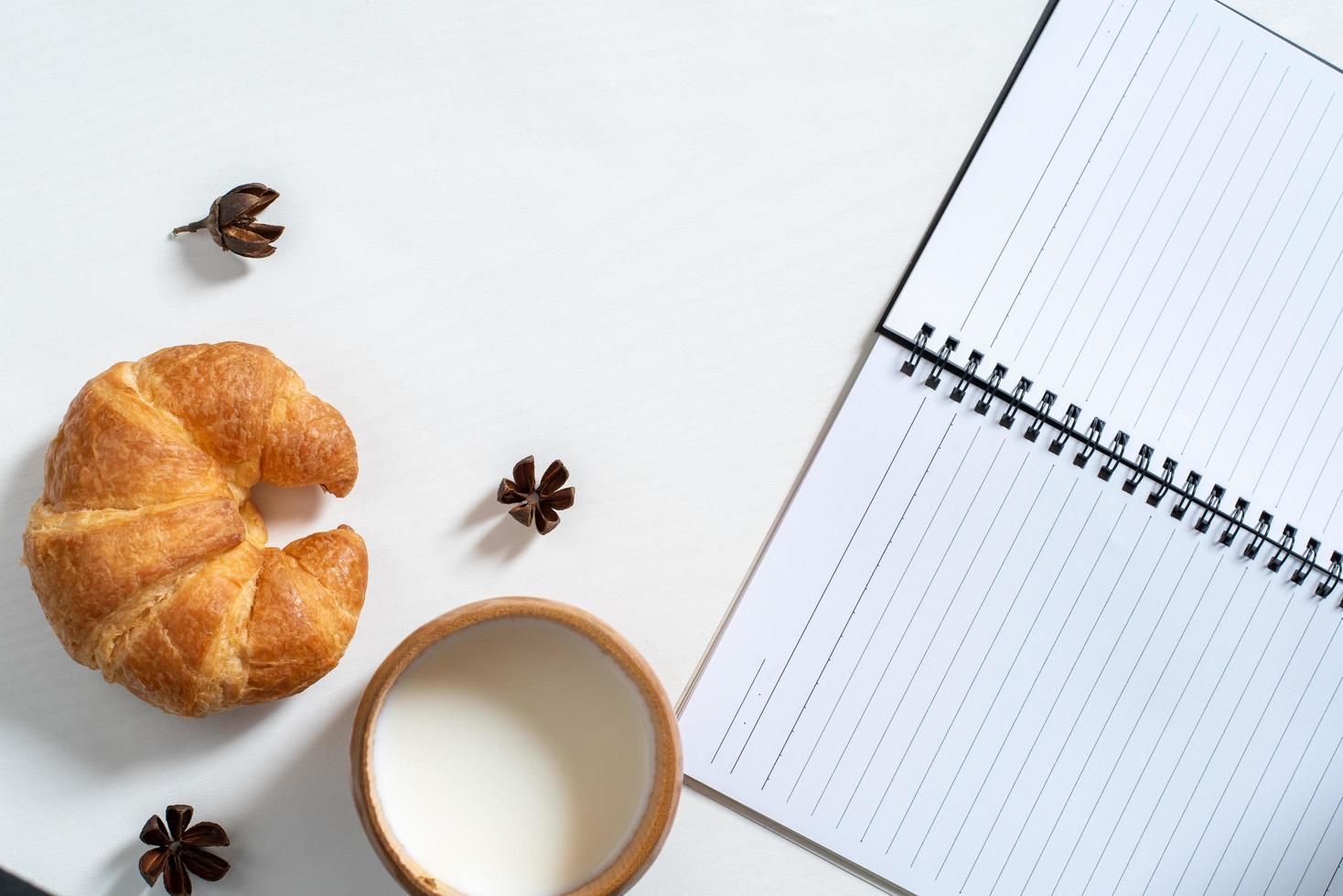 Top view of cup of milk, note book, croissant on wooden table photo