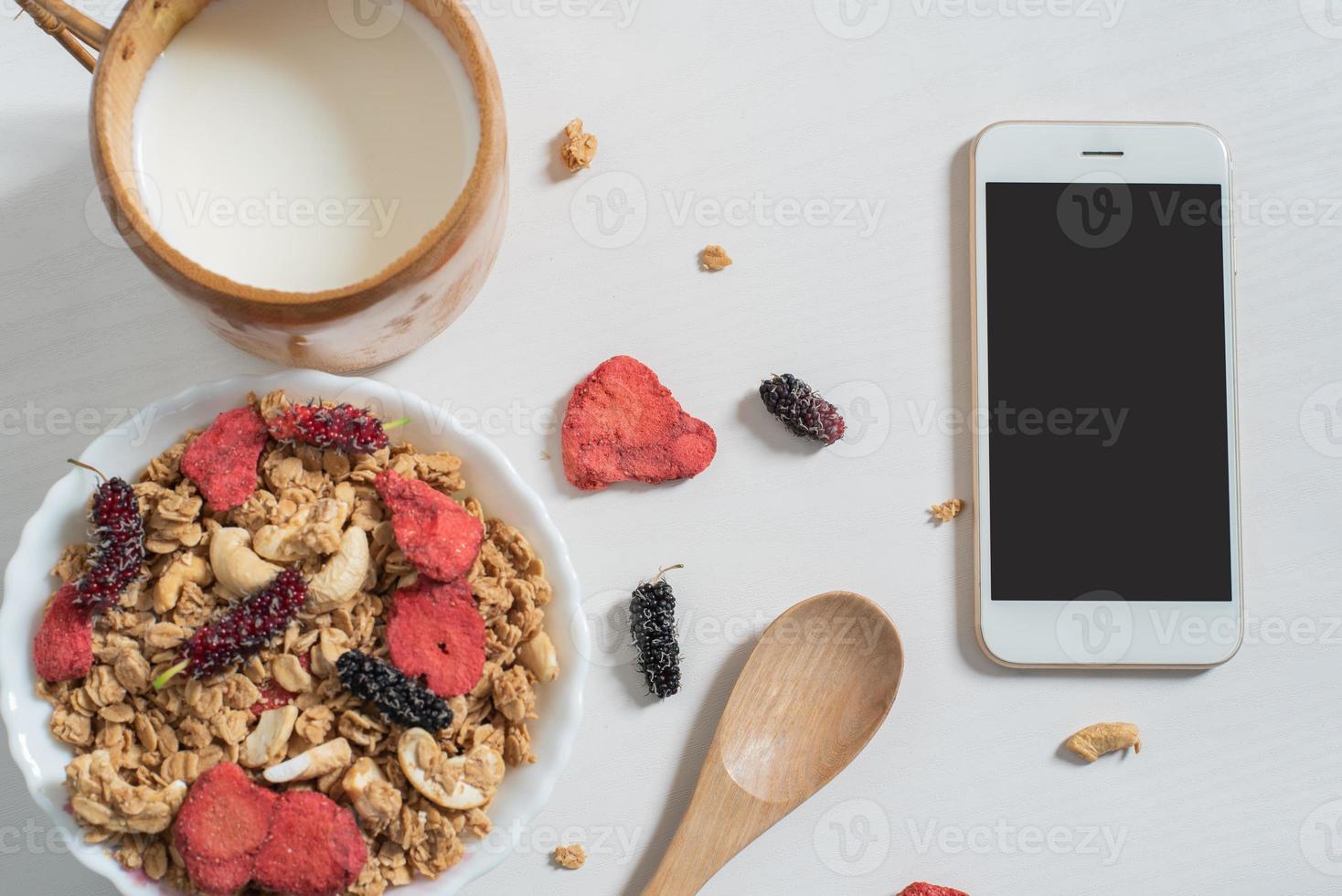 Top view of oat flakes with strawberry, mulberry, almond , milk and cellphone photo