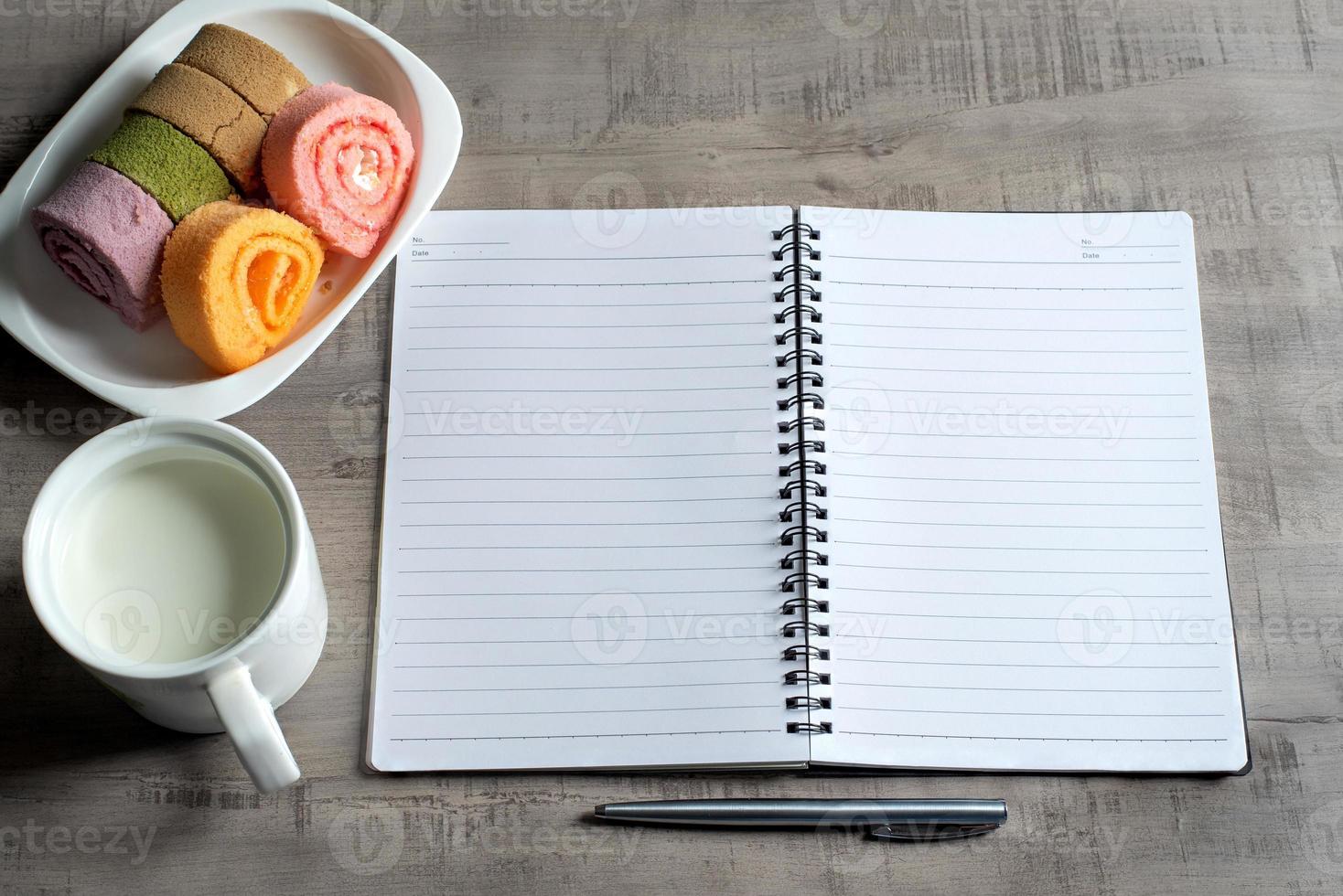 Top view of notebook, jam roll, cup of milk, pen on wooden, Business, education concept and design photo