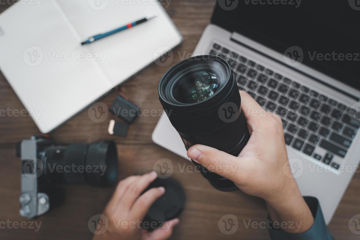 cierre la lente de la cámara en la mano un hombre y un equipo de fotografía en una mesa de madera vintage, concepto de trabajo fotográfico foto