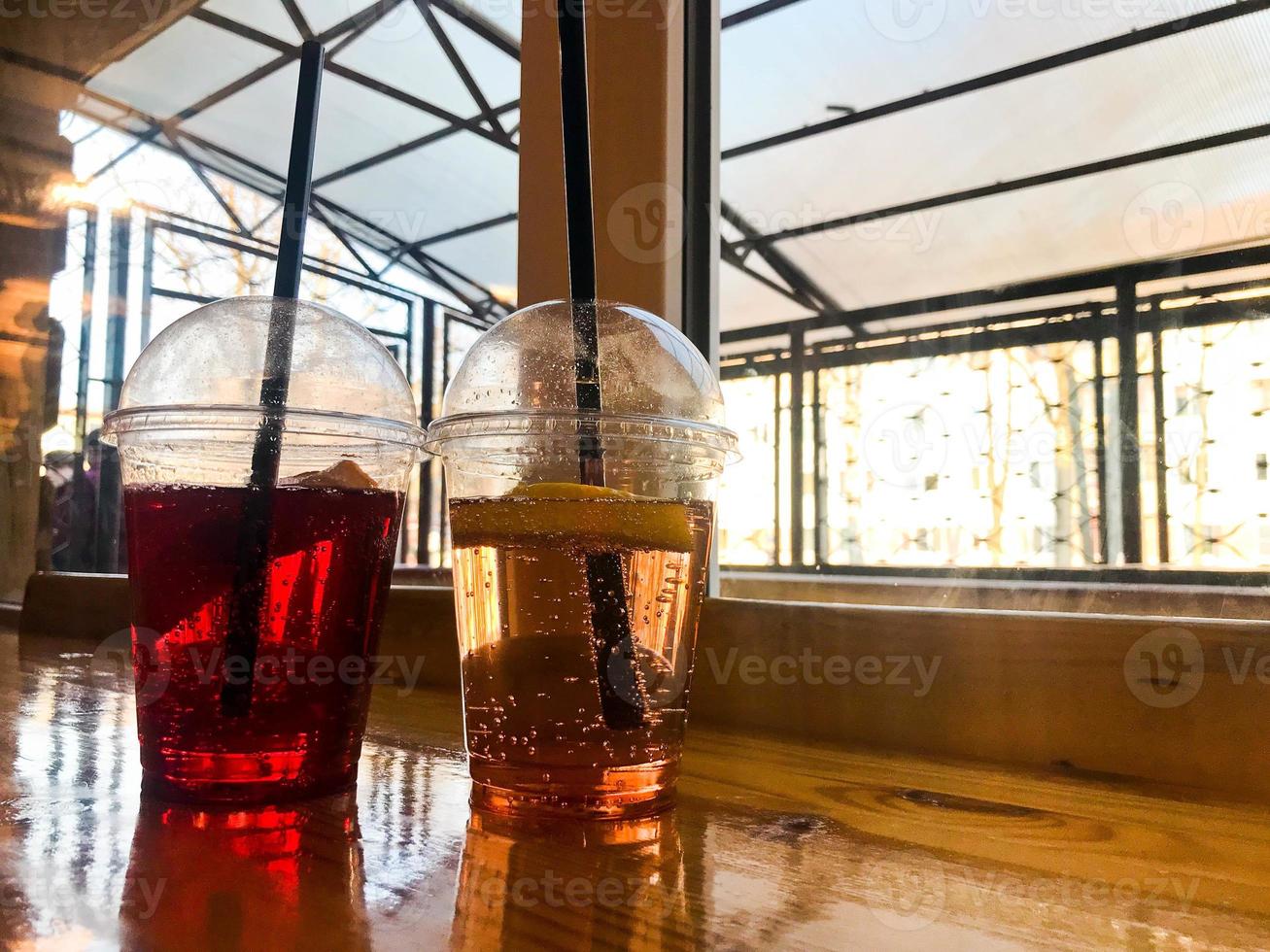 Two glasses of plastic red and yellow refreshing cold tasty sweet raspberry strawberry cherry orange peach lemon fruit lemonade natural with a straw and syrup bubbles photo