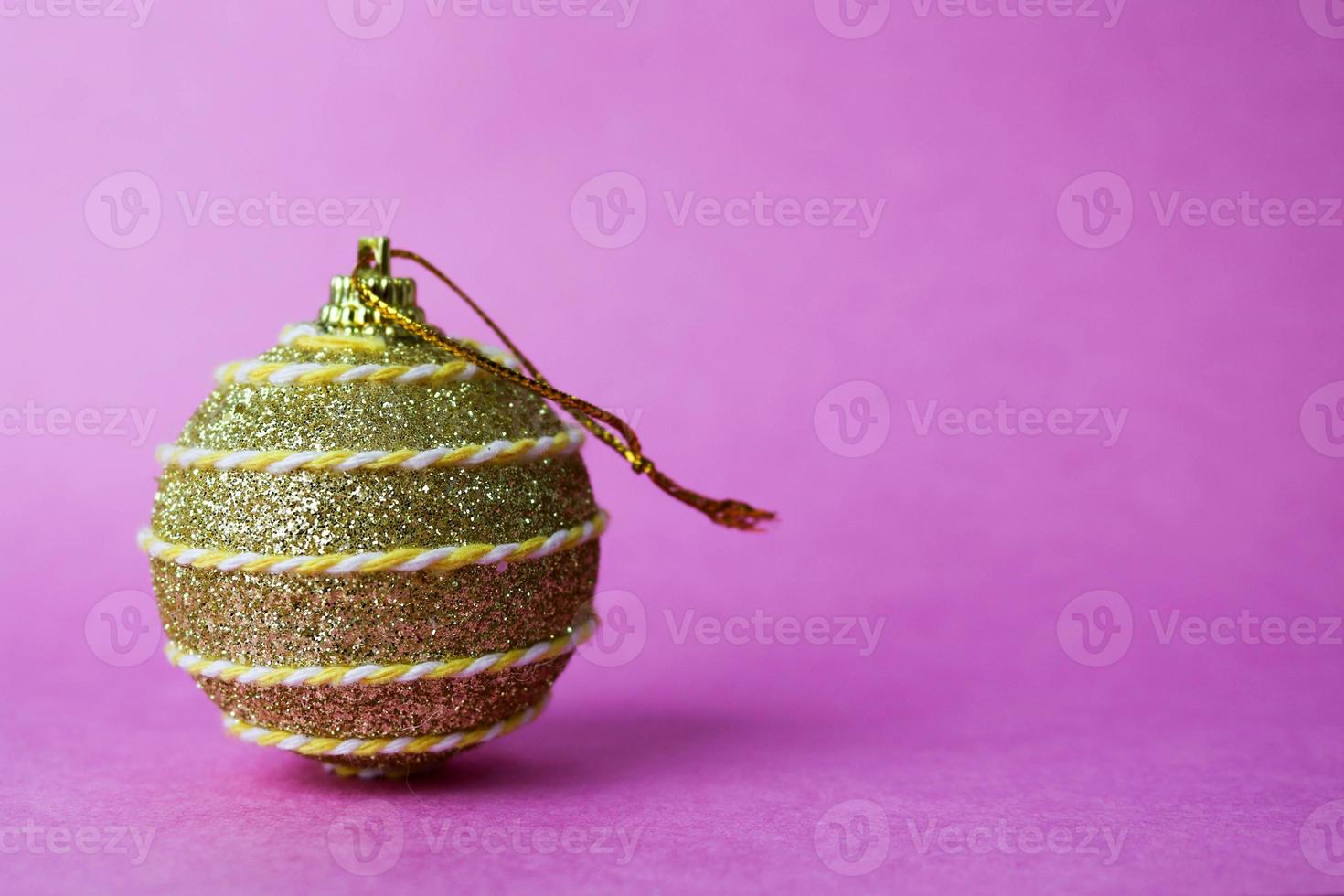 Golden yellow small round glass plastic winter smart shiny decorative beautiful xmas festive Christmas ball, Christmas toy pasted over with spangles on a violet pink background photo