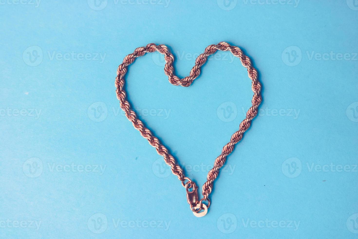 Texture of a beautiful golden dear festive chain of unique weaving in the shape of a heart on a blue background and copy space. Concept love, marriage proposal, marriage, St. Valentine's Day photo