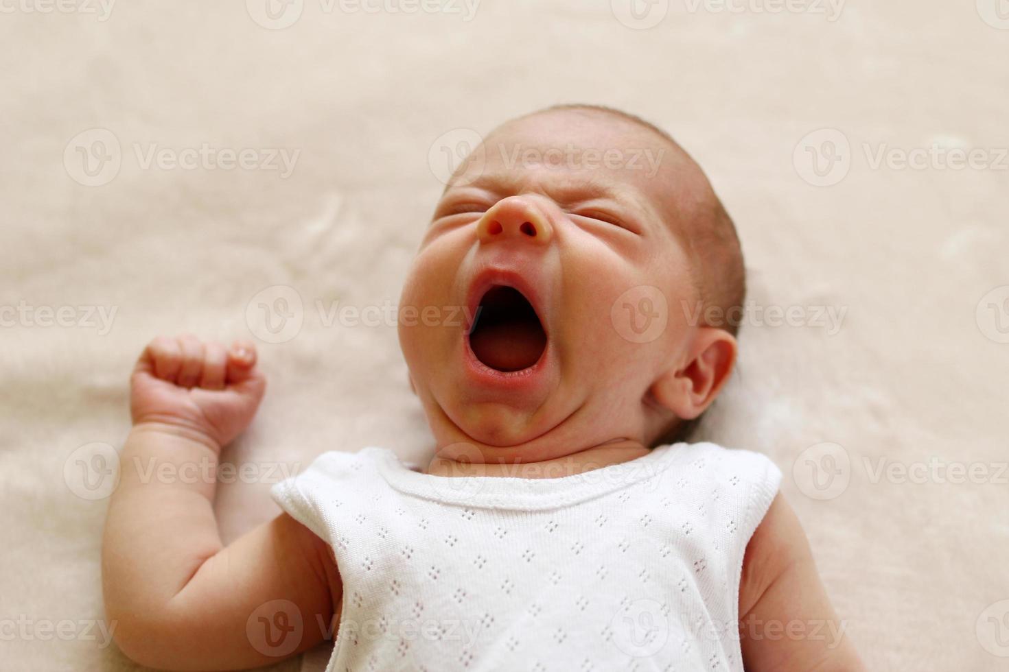 One month child is yawning lying on a blanket before go to sleep. photo