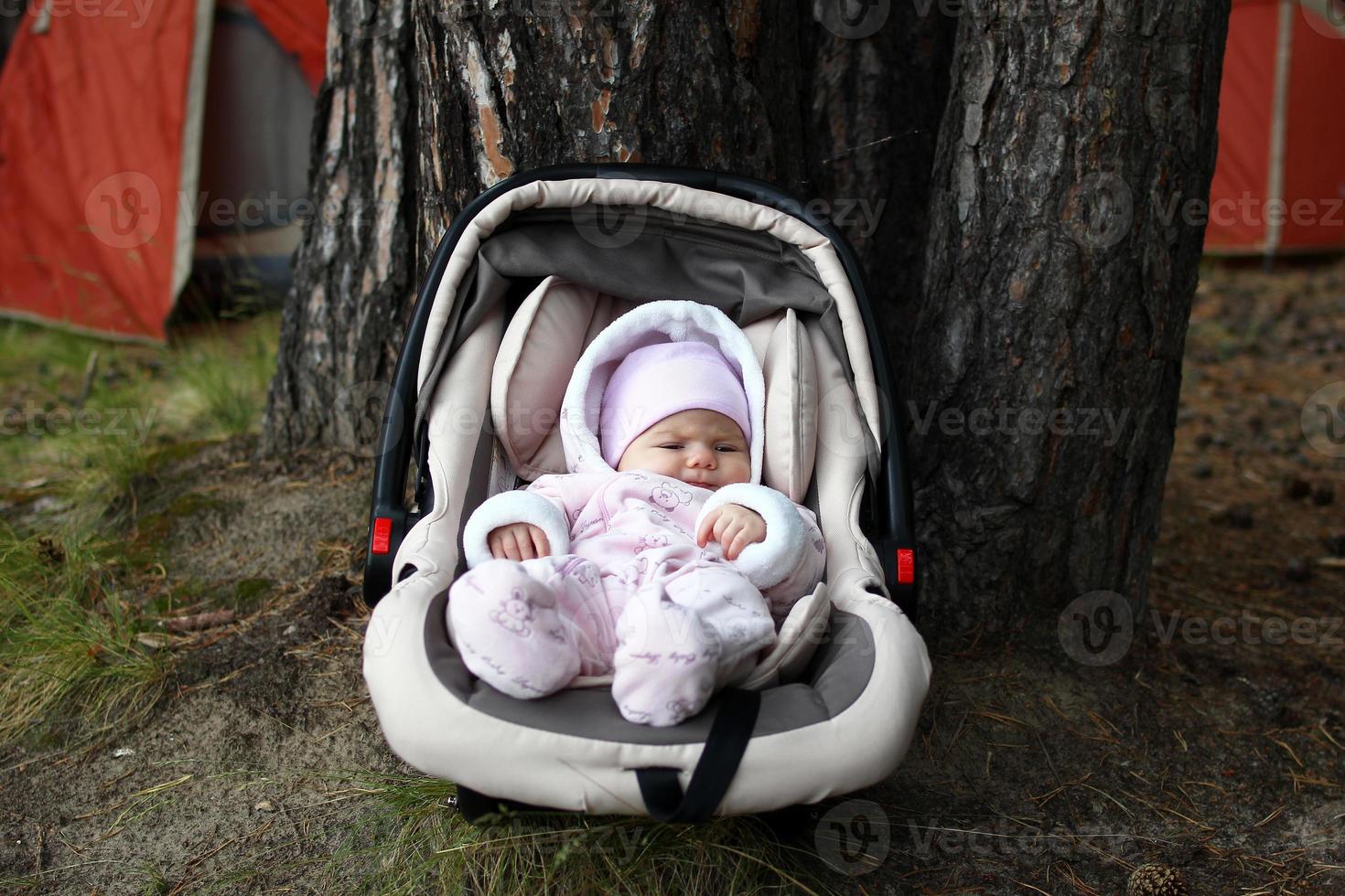 Little child in car seat near a tree on a background of tents photo